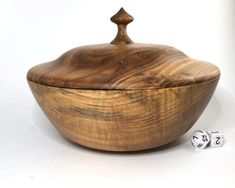 a wooden bowl sitting next to two dices on a white surface with the lid up