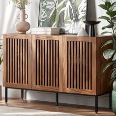 a sideboard with wooden slats on it in front of a painting and potted plants