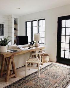 a desk with two computers on top of it in front of some black doors and windows