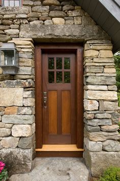 a wooden door with two lanterns on each side and stone walls around it, in front of a house