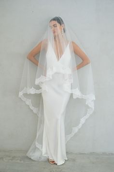 a woman in a white wedding dress with a veil on her head, standing against a wall