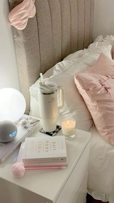 a bed with pink pillows and books on top of it next to a night stand