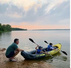 two people in a yellow kayak sitting on the edge of a body of water