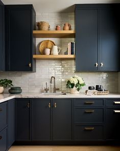 a kitchen with dark blue cabinets and white tile backsplash, gold pulls on the cupboards