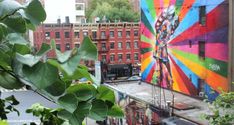 a large colorful mural on the side of a building next to trees and buildings with lots of green leaves