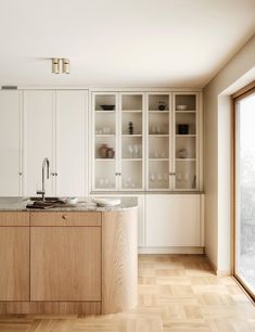 an empty kitchen with white cabinets and wood flooring on the walls, along with a large window