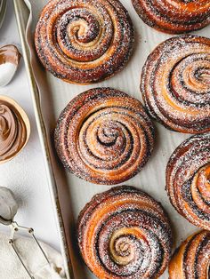 freshly baked cinnamon rolls on a baking sheet with icing and spoons next to them