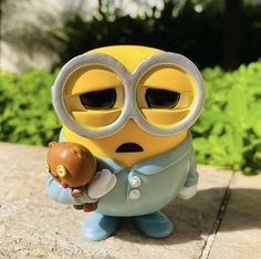 a yellow toy with big eyes holding a small object in his hand and wearing glasses