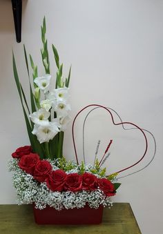 a vase filled with white and red flowers on top of a wooden table next to a heart shaped decoration