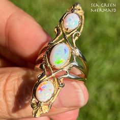 Welcome to Sea Green Mermaid! For sale is a 14k gold Australian opal navette ring designed by the respected Los Angeles jeweler Walton & Co., specialists in Art Nouveau jewelry from 1900 to 1920. The ring features three Australian opal cabochons set north-south along the front of this two inch tall navette ring. The opals are subtle in dim light, and flash with colorful pin-fire in bright sunlight or artificial light. You will see lots of purple, neon green, blue, and red fire as you move the ring in the sunlight. The mounting itself has an elegant filigree design with a trio of leaves at the top and bottom. The wide triple shank narrows to a single thick band in the back of the ring. The opals are visible from the interior of the ring. You might expect to find this ring in the jewelry box Navette Ring, Opal Art, Dim Light, Purple Neon, Nouveau Jewelry, Green Mermaid, Artificial Light, Art Nouveau Jewelry, North South