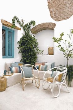 two white chairs sitting on top of a patio next to a tree and potted plant