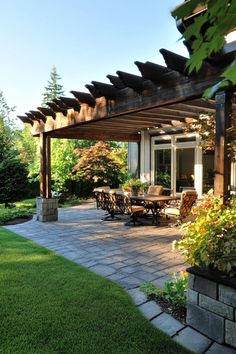 Outdoor patio with pergola and dining table surrounded by lush greenery. Covered Pergola Attached To House, Captain Claw, Covered Patios Attached To House, Covered Pergola Patio, Patio Cover Ideas, Cobblestone Patio, Backyard Decks