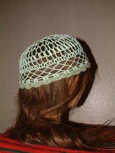 a woman wearing a green crochet hat with long brown hair in front of a white wall