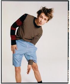 a young man is posing with his hands on his hips while wearing shorts and a sweater