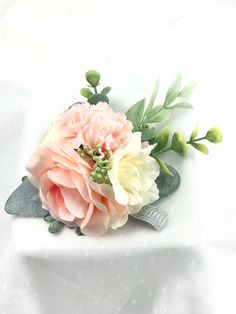 a pink and white flower sitting on top of a white cloth covered tablecloth with green leaves