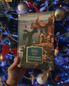 a person holding up a book in front of a christmas tree