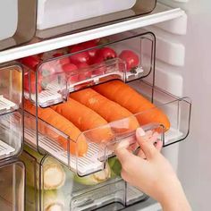 the person is taking carrots out of the refrigerator with clear containers on both sides