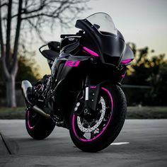 a black and pink motorcycle parked in a parking lot next to some tree's