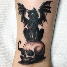 a skull and bat tattoo on the leg with a dragon sitting on top of it