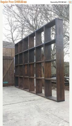 a large wooden bookcase sitting on top of a cement ground next to a tree