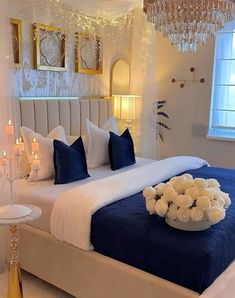 a large bed with blue and white sheets, candles and flowers on the headboard