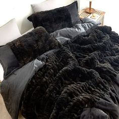 a bed covered in black fur with pillows and blankets on it's headboard