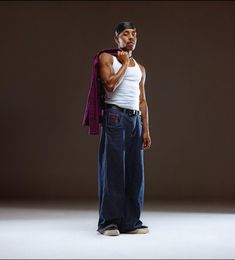 a man in white tank top and blue jeans standing with his hand on his chin