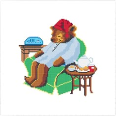 a cross stitch bear sitting on a chair with a tea cup and saucer in his lap