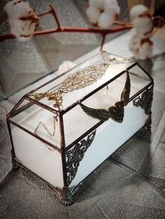 a glass box that has some kind of jewelry inside of it on a table with cotton flowers in the background