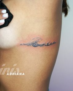 a woman's stomach with a wave tattoo on her left side ribcage