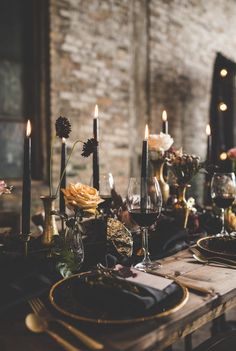 the table is set with black and gold place settings, candles, and flowers in glass vases