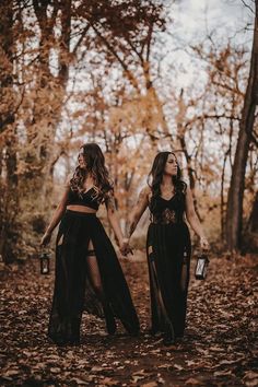 two women holding hands and walking through the woods in black outfits with long sheer skirts