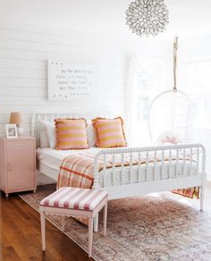 a white bed sitting on top of a wooden floor next to a pink chest of drawers