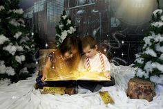 two children are reading a book in front of christmas trees and snow covered ground with lights