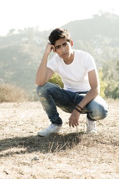 a young man sitting on top of a dry grass covered field next to a forest