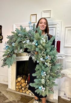 a woman standing in front of a fireplace holding a christmas wreath