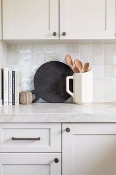 a kitchen counter with white cabinets and wooden utensils in a black frying pan