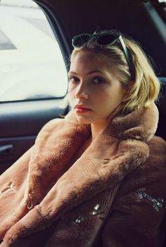 a woman sitting in the back seat of a car wearing sunglasses and a fur coat