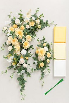 yellow and white flowers with green stems on a white surface next to a piece of paper