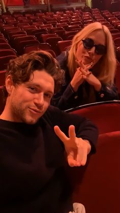 a man and woman sitting in an auditorium giving the peace sign