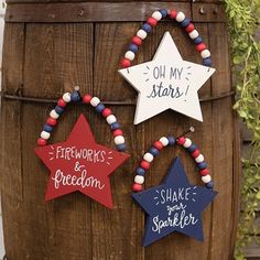 three wooden stars are hanging on a barrel with red, white and blue beaded bracelets