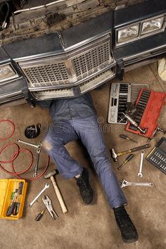 a man laying on the ground with tools under his car