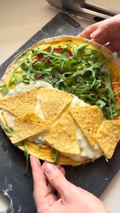 a person is placing tortilla chips on top of a pizza with cheese and arugula