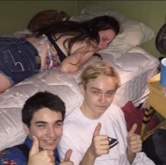 three people laying on a bed giving thumbs up