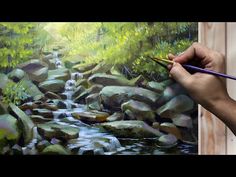 a person is holding a paintbrush in their hand while painting a landscape with rocks and water