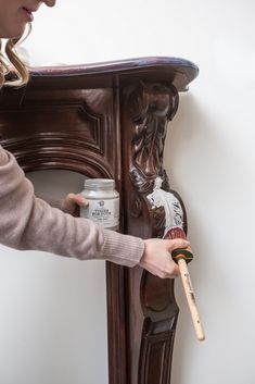 a woman is holding a paintbrush and painting the side of a wooden cabinet