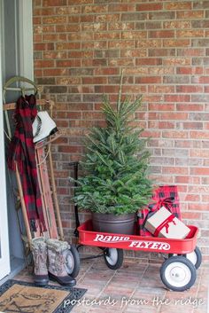 a christmas tree sitting on top of a red wagon next to a brick wall and door