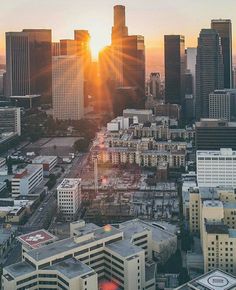 the sun is setting over a city with tall buildings and skyscrapers in the foreground