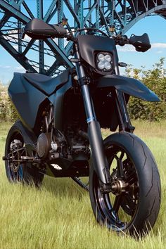 a black motorcycle parked in the grass under a bridge