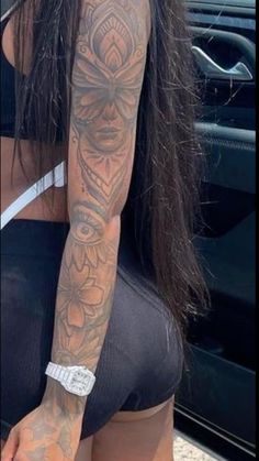 a woman with long hair and tattoos on her arm standing in front of a car